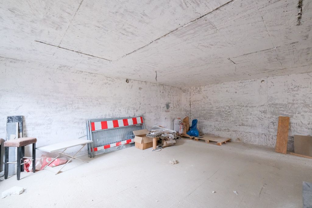 Leerer, unvollständig gebauter Raum mit rotem und weißem Baustellenschutzzaun, Kartons und Holzpaletten an einer Wand.