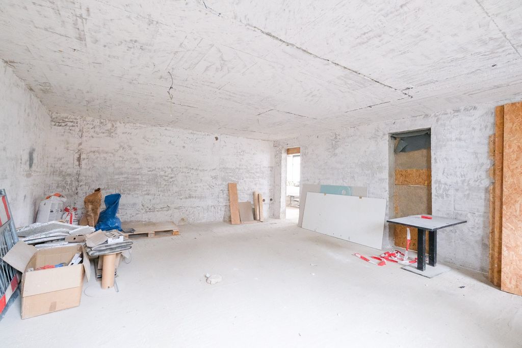 Leerer Raum in einem unrenovierten oder im Bau befindlichen Gebäude mit unverputzten Wänden und Bauutensilien in den Ecken.