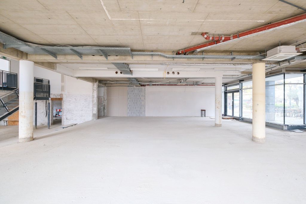 Leerer, heller Rohbau mit Betonsäulen, freiliegenden Leitungen und großen Fensterfronten in einem Neubau.