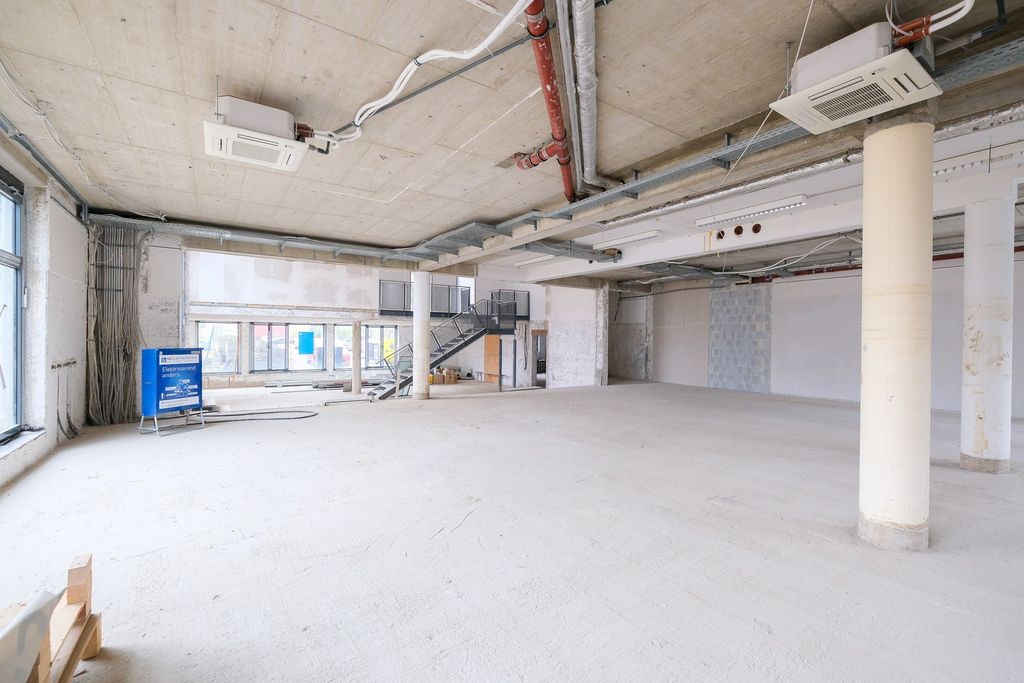 Großer, leerer Innenraum einer Baustelle mit sichtbarem Betondecken, Säulen und großen Fenstern.
