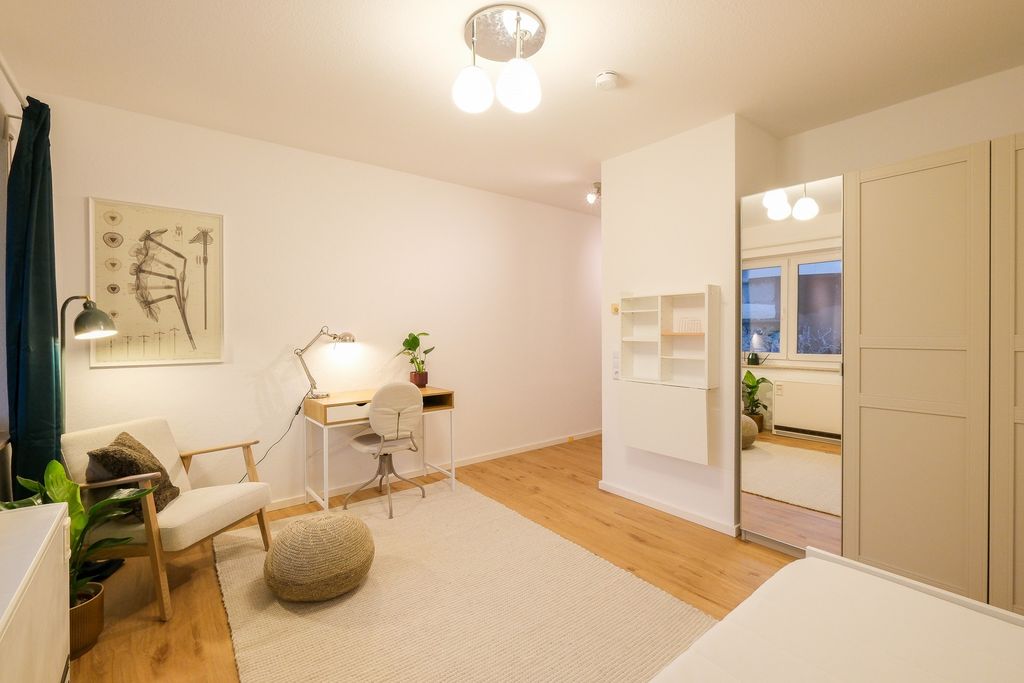 Helles, minimalistisches Arbeitszimmer mit weißem Schreibtisch, Stuhl, Lesesessel und großem Spiegel an der Wand, mit Holzboden und cremefarbenem Teppich.