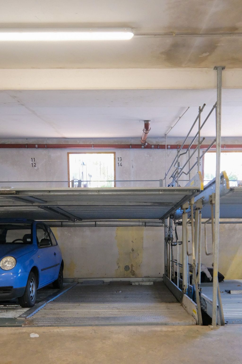 Blaues Auto in einer mehrstufigen Parkanlage mit Wagenheberplattformen und einem Fenster im Hintergrund.