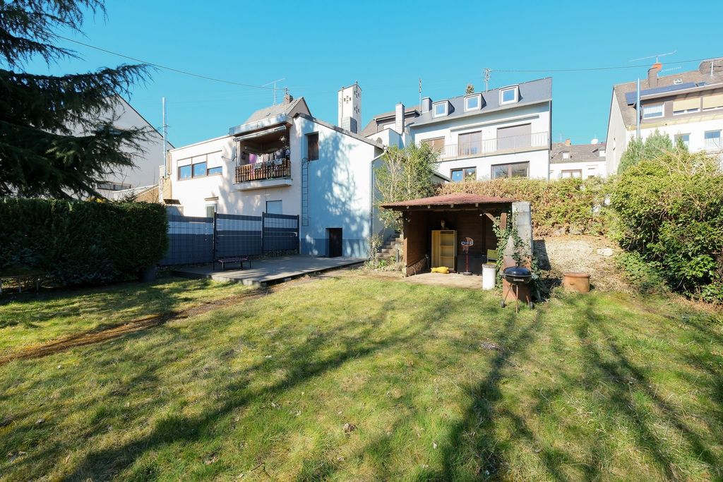 Ein weitläufiger Garten mit grünem Rasen, umgeben von hohen Hecken und mehreren Wohngebäuden im Hintergrund bei klarem Himmel.