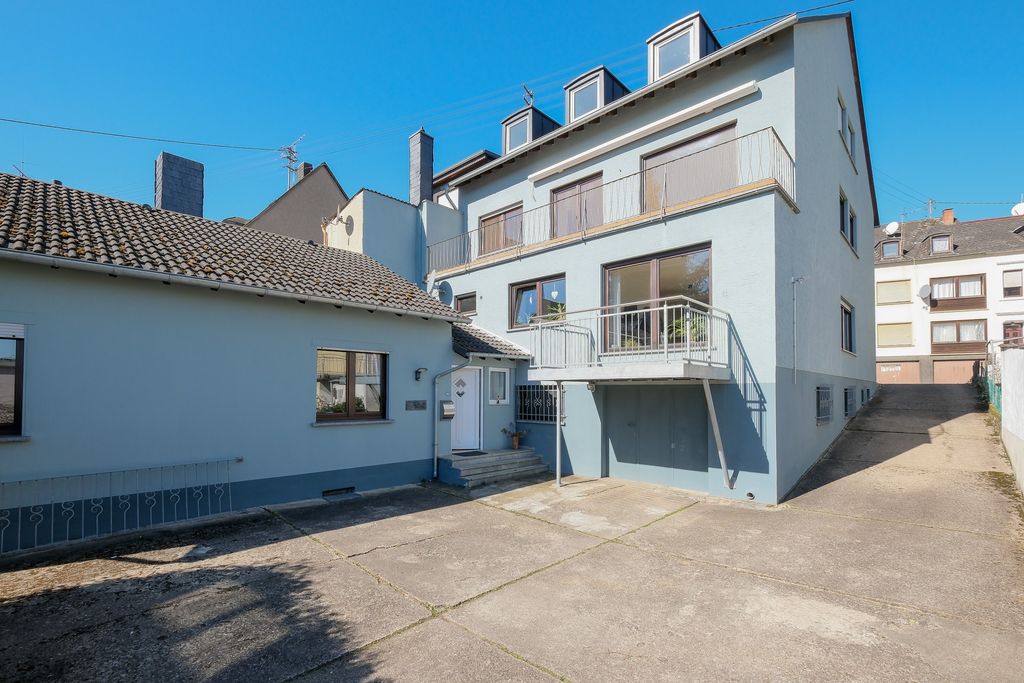 Mehrstöckiges Wohnhaus mit hellblauer Fassade und kleinem Balkon, umgeben von weiteren Gebäuden unter blauem Himmel.
