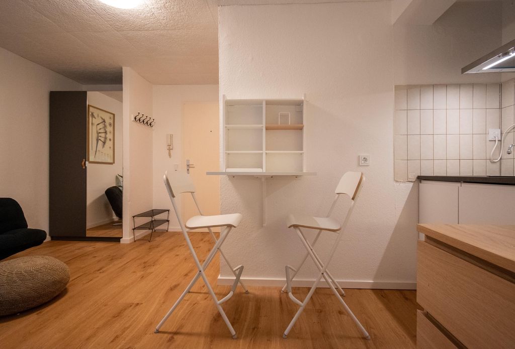 Zwei weiße Klappstühle vor einer kleinen Wandregal-Anrichte in einem modernen Raum mit Holzfußboden.