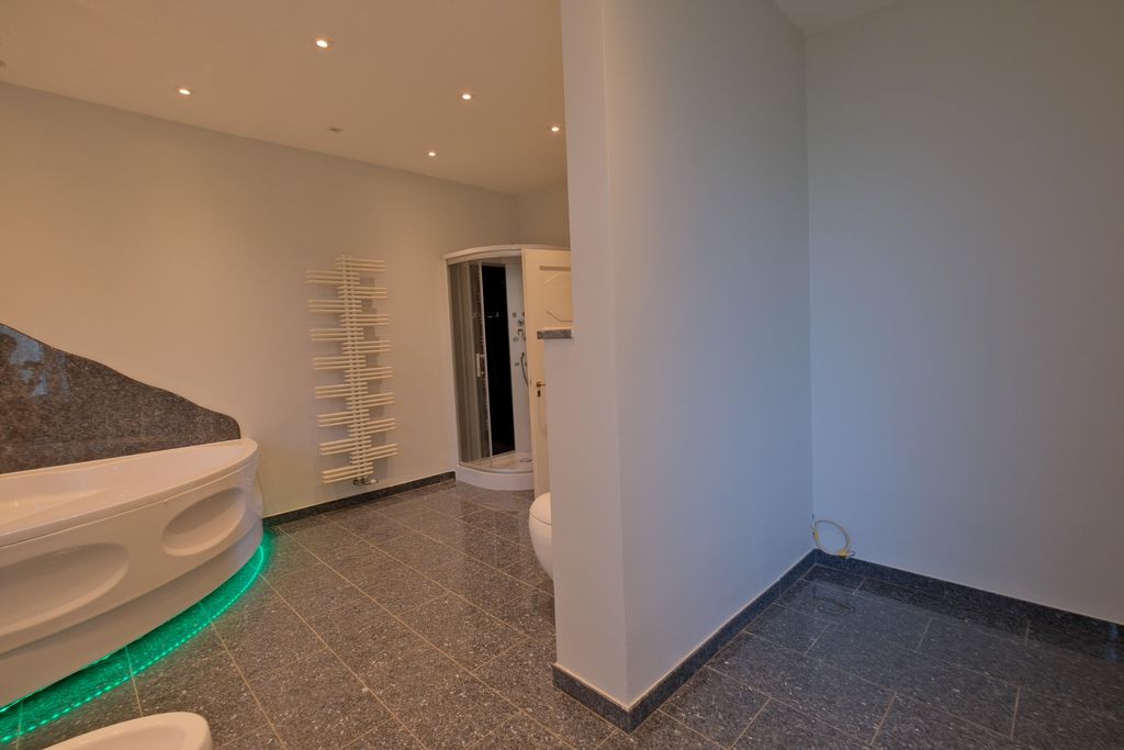 Modernes Badezimmer mit Eckbadewanne mit grüner LED-Unterbeleuchtung, Glastür-Dusche und weißem Heizkörper an der Wand.