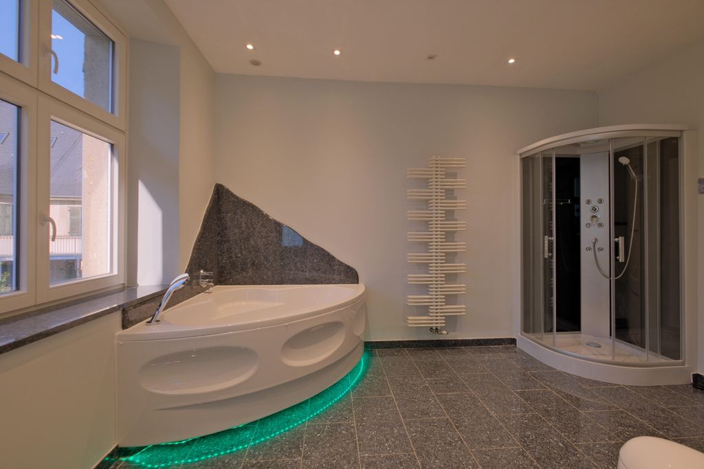 Ein modernes Badezimmer mit einer abgerundeten Badewanne mit grünem LED-Licht unter der Wanne, einer Dusche mit Glastüren und einem weißen Heizkörper an der Wand.