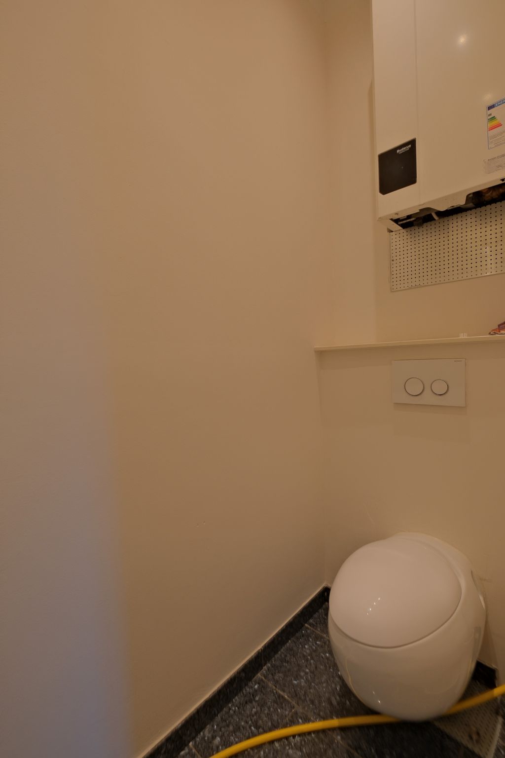 Moderne Toilette mit einem runden, weißen Design in einem kleinen Badezimmer mit beigen Wänden und schwarzem Bodenbelag.