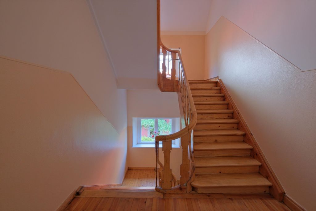 Innenraum einer Treppe mit Holzboden und Holzgeländer, weiße Wände und ein Fenster mit Blick nach draußen.