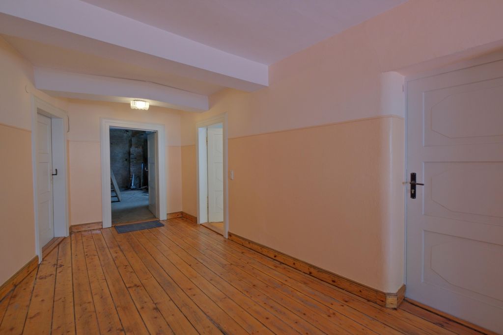 Ein heller Flur mit Holzboden und mehreren weißen Türen, eine Tür führt in einen dunkleren Raum.