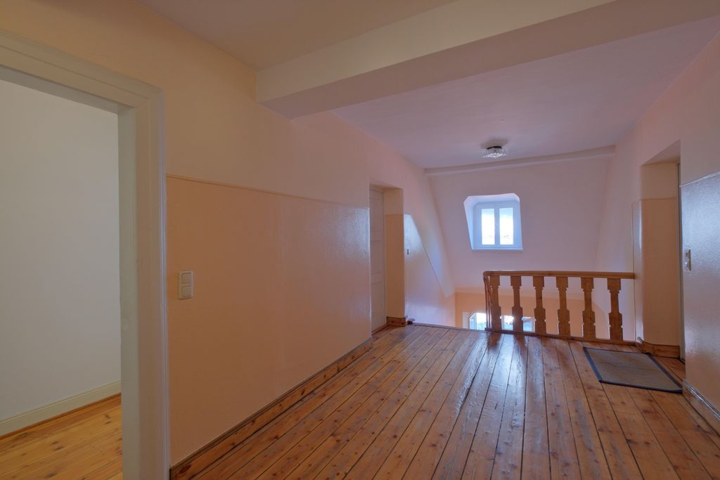 Flur mit Holzboden und hellen, pastellfarbenen Wänden in einem älteren Haus mit Treppe und Fenster am Ende.