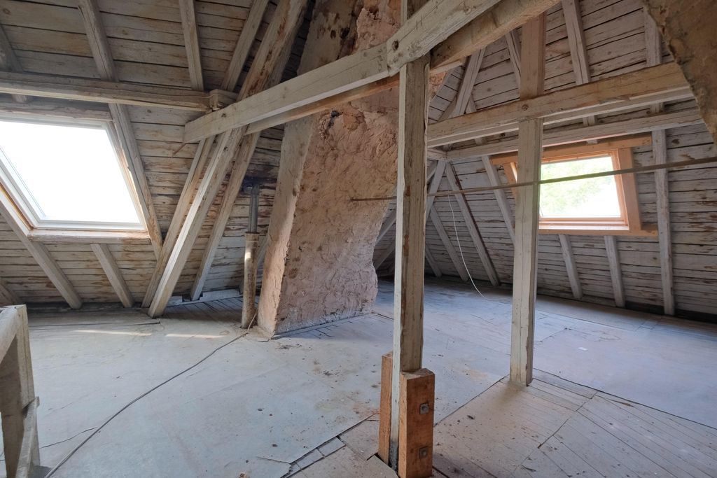 Leerer Dachboden mit sichtbaren Holzbalken, Holzverkleidung und zwei großen Dachfenstern, die Tageslicht hereinlassen.