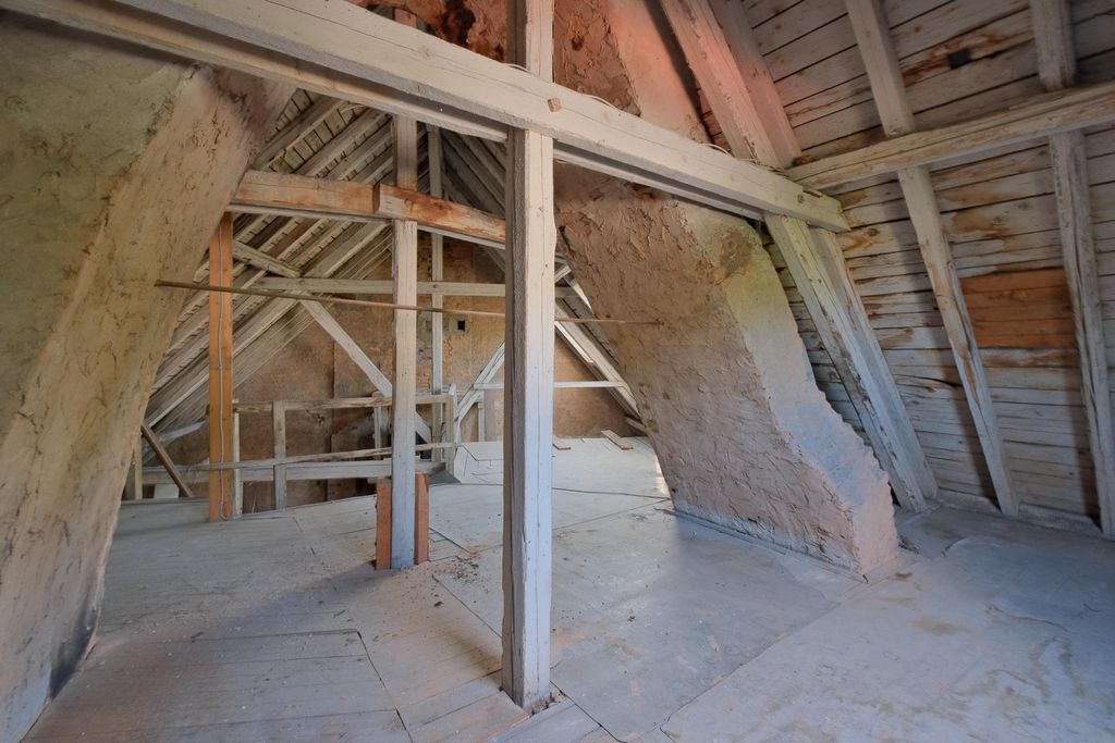 Alter, leerer Dachboden mit sichtbaren Holzbalken und schrägen Wänden aus Holz und Putz.