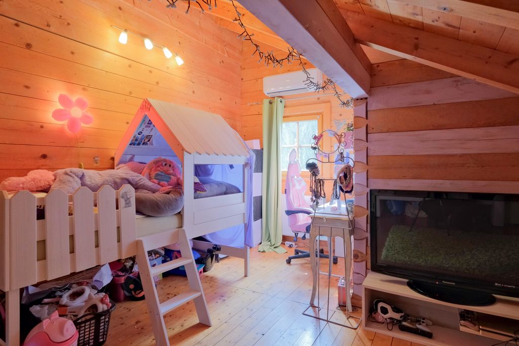Kinderzimmer mit einem Holz-Hochbett in Form eines Hauses, warm beleuchtet mit einer Blume-Wandlampe, einem Schreibtisch mit Stuhl am Fenster und einem großen Fernseher im Raum.