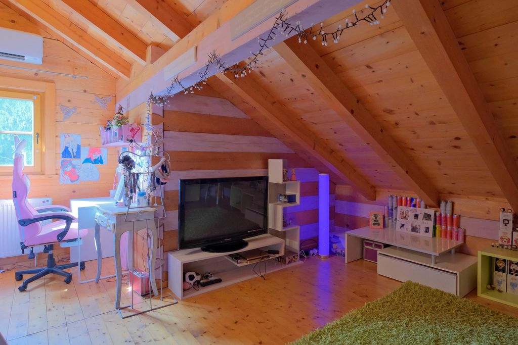 Ein gemütlicher Dachbodenraum mit Holzverkleidung, der eine pinke Bürostuhl, einen Schreibtisch mit Zeichnungen und einen Fernseher auf einem weißen TV-Ständer enthält.