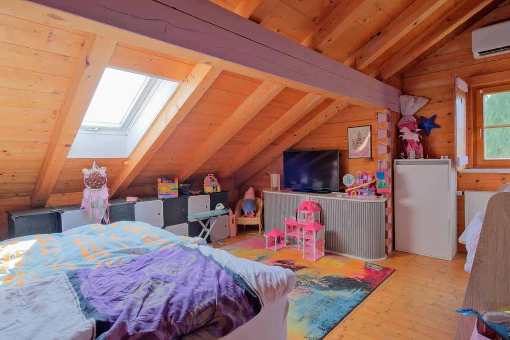 Kinderzimmer auf dem Dachboden mit Holzverkleidung, Dachfenster, buntem Teppich und verschiedenen Spielzeugen und Möbeln.