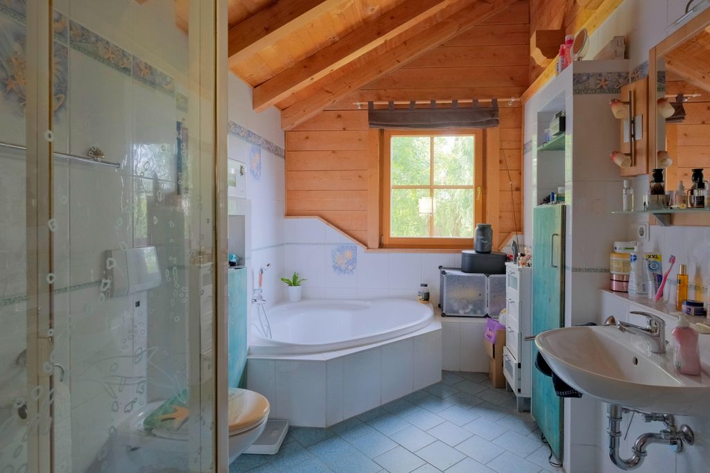 Helles Badezimmer mit Holzdecke, Eckbadewanne unter einem Fenster, Waschbecken und Dusche.