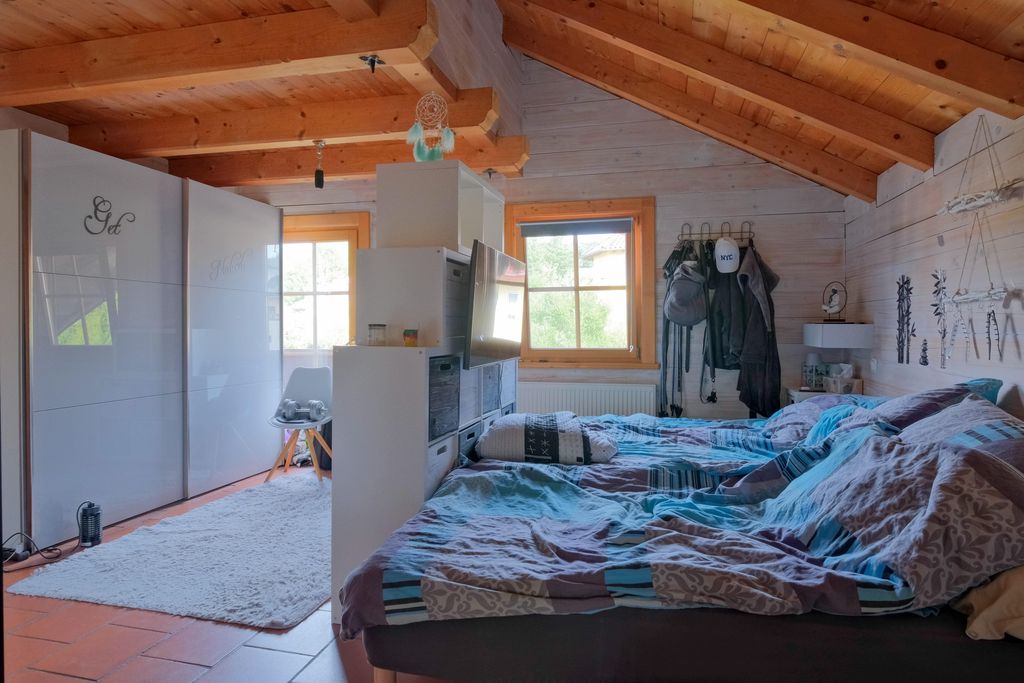 Ein gemütliches Schlafzimmer mit Holzbalkendecke, zwei Betten mit gemusterten Bettdecken und weißen Schiebetüren mit Spiegel an einer Wand.
