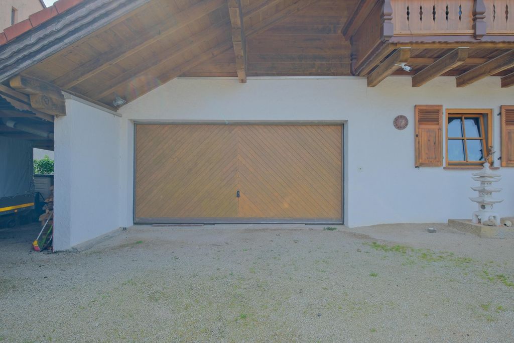 Weiße Garage mit einem großen, hölzernen Doppeltor und Fenster mit Holzläden in einem Haus mit sichtbarer Holzbalkendecke.