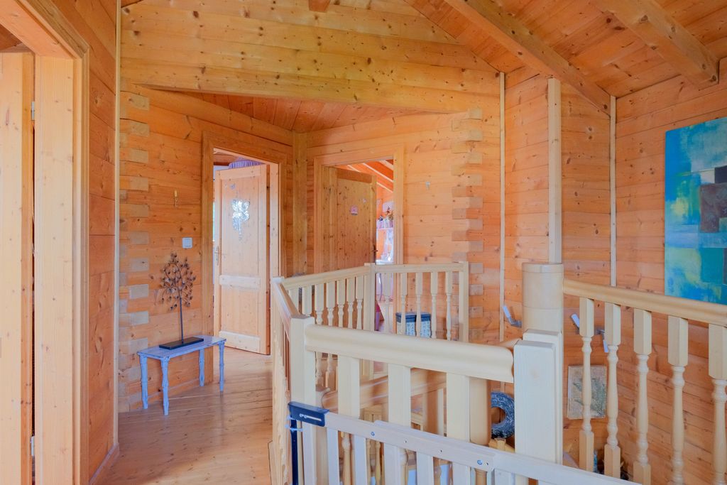 Innenraum eines Hauses mit naturbelassenen Holzwänden und Holzboden, Treppengeländer aus hellem Holz und einer kleinen blauen Bank mit einer Metallskulptur eines Baumes.