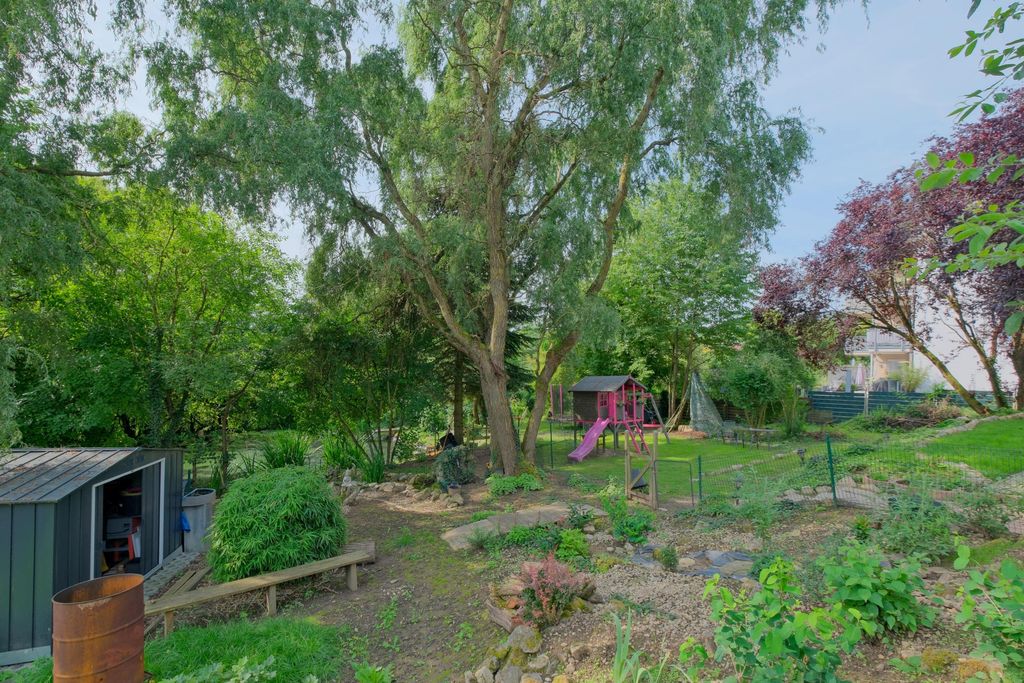 Garten mit vielen Bäumen, einem kleinen Spielhaus mit Rutsche, einem Geräteschuppen und einem Weg, der durch die grüne Fläche führt.