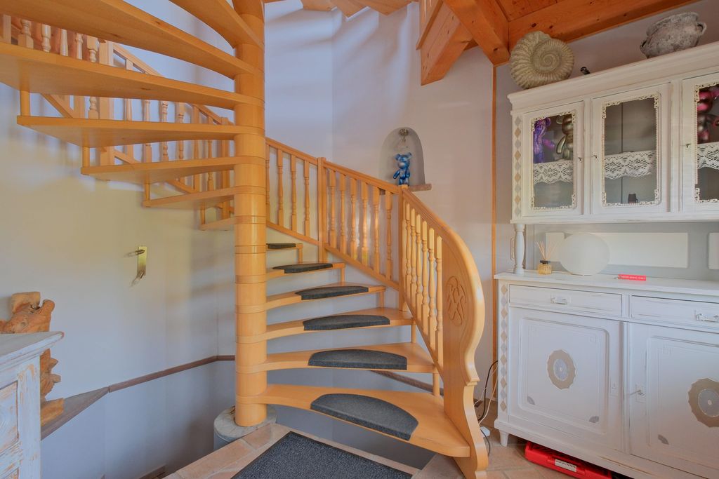 Eine hölzerne Wendeltreppe mit Teppichmatten auf den Stufen in einem Raum mit weißen Wänden und einem weißen alten Schrank.
