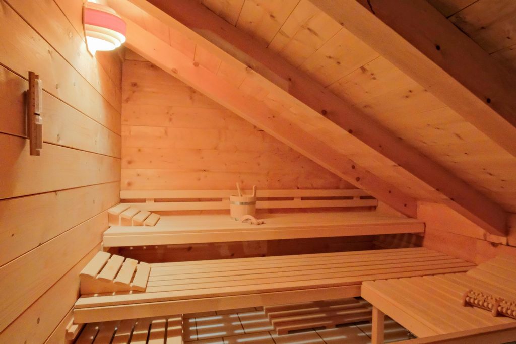 Innenansicht einer kleinen Sauna mit schräger Decke und Holzbänken, beleuchtet von einer Wandlampe.