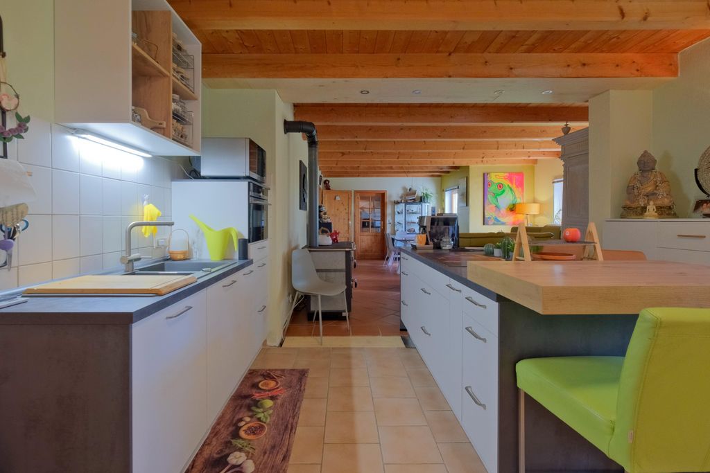 Moderne Küche mit weißen Schränken, Holzdecke und grünem Stuhl vor einer Arbeitsplatte mit Holzauflage.