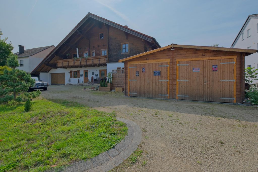 Großes traditionelles Haus mit Balkon und doppelter Holztür-Garage auf einem geschotterten Hof mit Rasenfläche im Vordergrund.