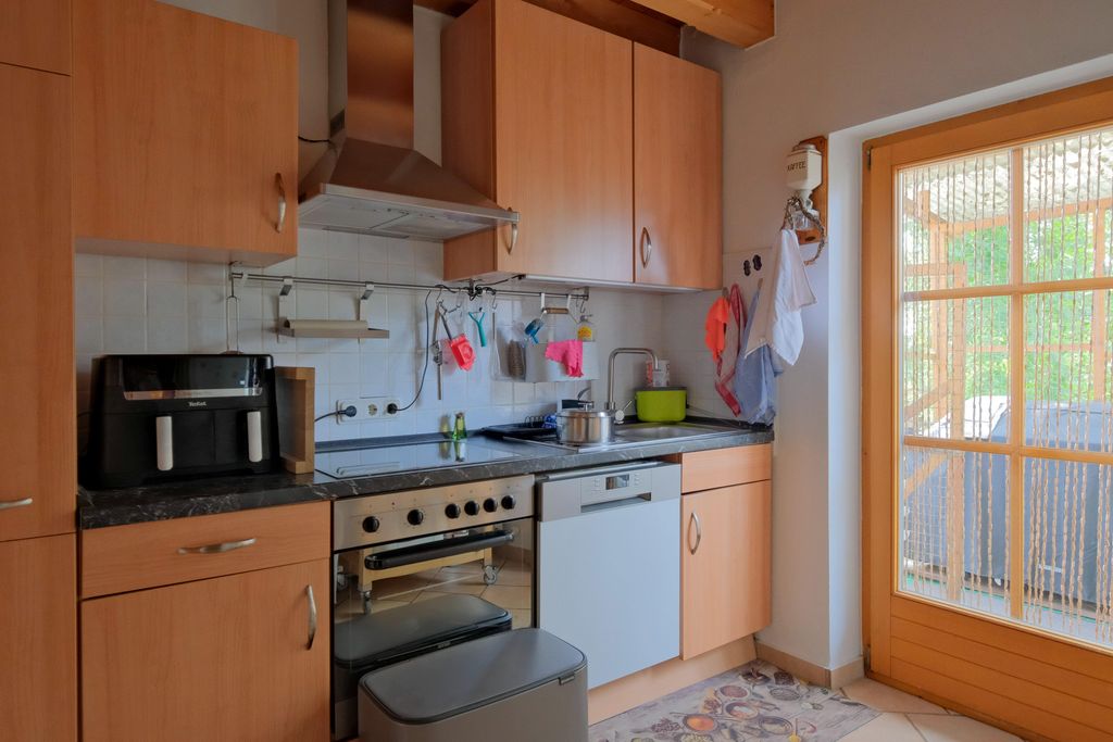 Moderne Küche mit Holzschränken, einem Herd mit Backofen, einer Kaffeemaschine und einer Glasschiebetür mit Blick auf eine Terrasse.