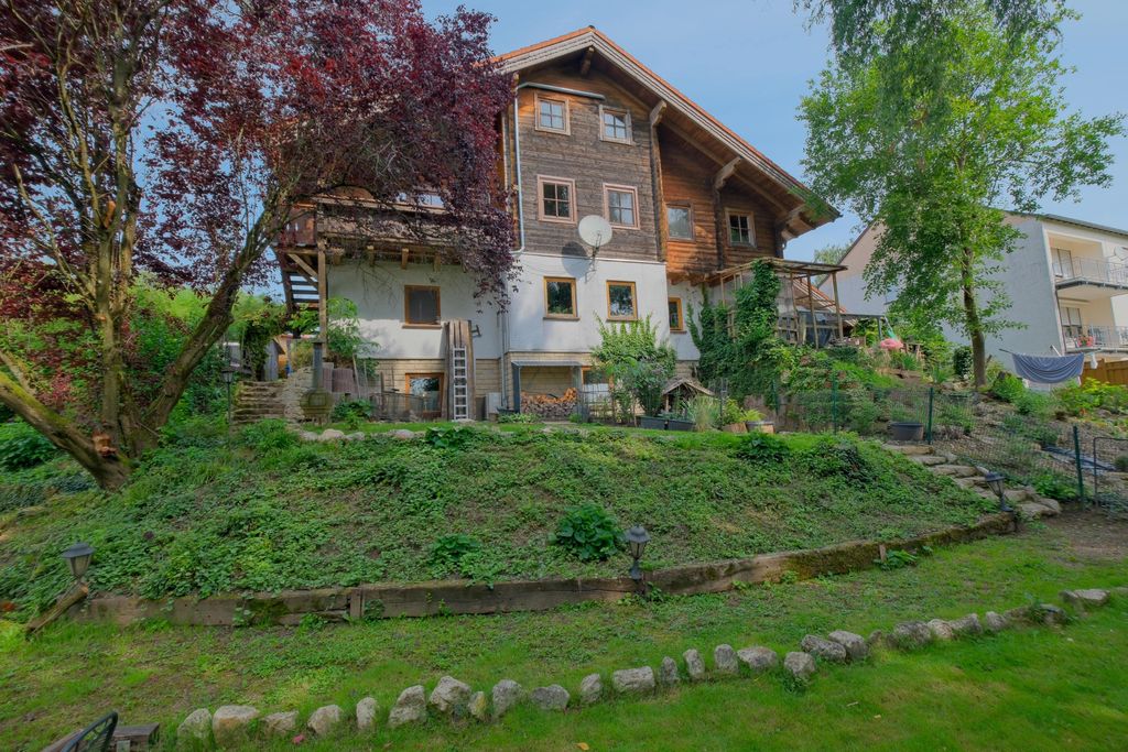 Ein zweistöckiges Haus mit Holzverkleidung und mehreren Fenstern, umgeben von Bäumen und einem gepflegten Garten mit steinernem Weg und Pflanzen.
