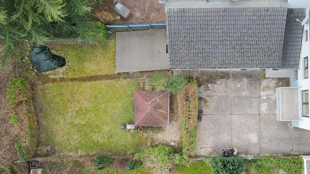 Drohnenansicht eines kleinen Gartens mit einem Pavillon in der Mitte, einem Teich auf der linken Seite und einem Haus mit Schornstein rechts.