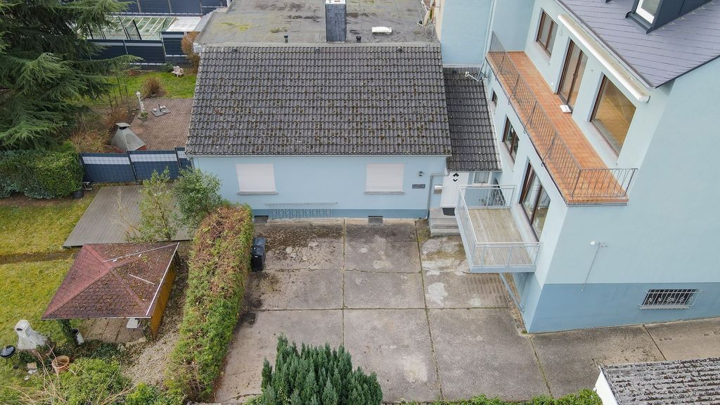 Vogelperspektive auf ein blaugraues Wohnhaus mit Balkon und einer angrenzenden Garage, umgeben von einem begrünten Garten und gepflastertem Hof.