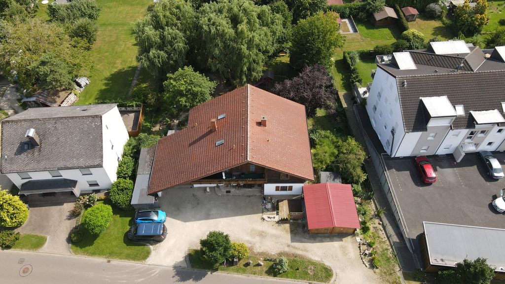 Luftaufnahme eines Einfamilienhauses mit rotem Dach, umgeben von Bäumen und mehreren geparkten Autos auf einem kleinen Grundstück in einer Wohngegend.