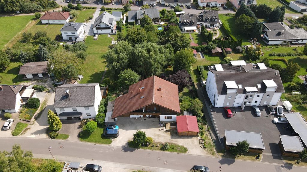Luftaufnahme eines Wohngebiets mit Einfamilienhäusern, Gärten und Autos entlang einer Straße an einem sonnigen Tag.