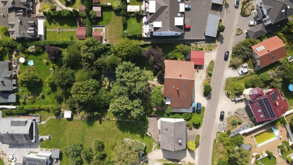 Luftaufnahme eines ruhigen Wohngebiets mit Einfamilienhäusern, bepflanzten Gärten und einer Straße mit parkenden Autos.