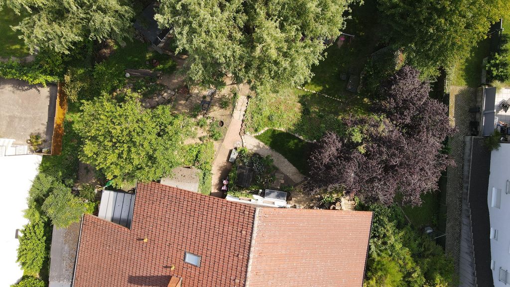Vogelperspektive eines Gartens mit mehreren Bäumen und einem Haus mit rotem Ziegeldach, das einen Teil des Bildes einnimmt.