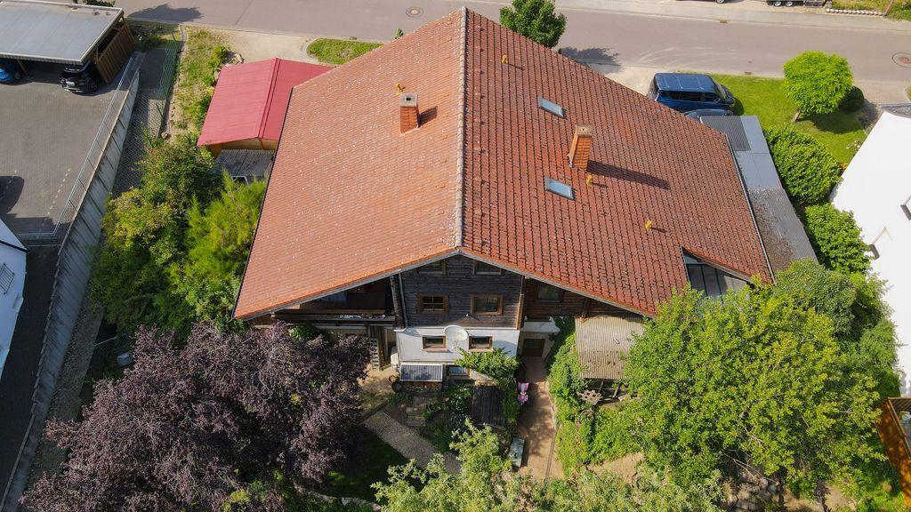 Luftaufnahme eines Wohnhauses mit rotem Ziegeldach, umgeben von Bäumen und einem Garten, an einer Straße mit geparkten Autos.