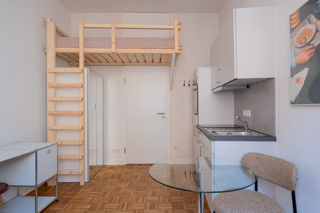 Kleine, moderne Wohnung mit einem Hochbett aus Holz, Glas-Tisch und Küchenzeile mit weißen Schränken.