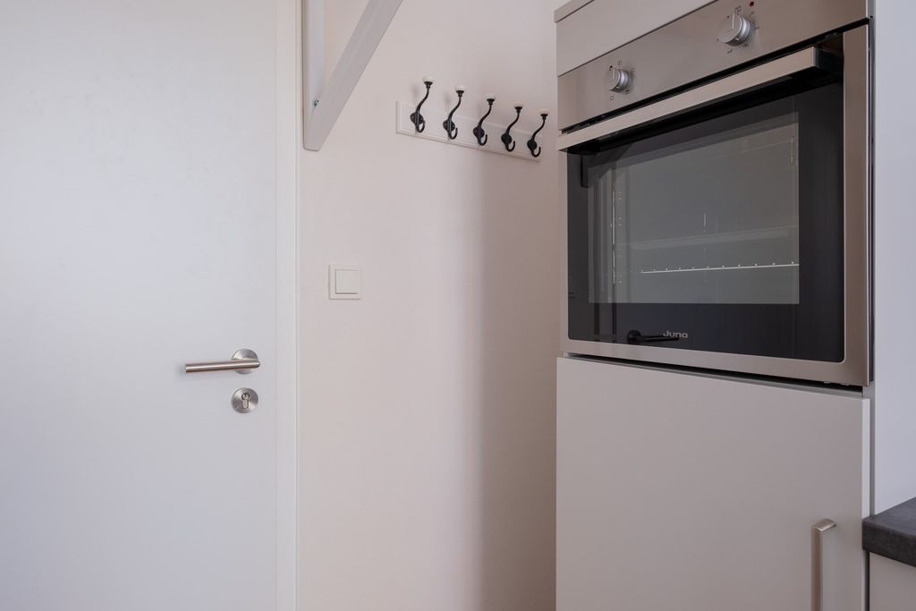 Moderner eingebauter Backofen in einer weißen Küche neben einer weißen Tür mit mehreren Haken an der Wand.