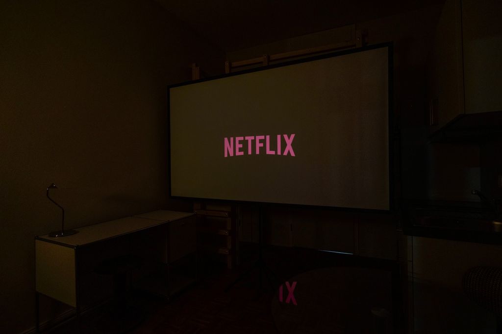 Ein dunkler Raum mit einem großen Bildschirm, auf dem das Wort "Netflix" in rosa Buchstaben angezeigt wird.