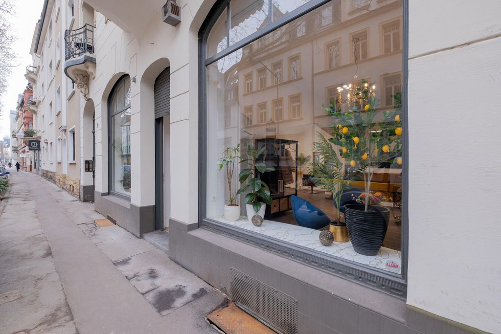 Eine Straße mit Altbauten und einem Schaufenster, das verschiedene Pflanzen in Blumentöpfen zeigt, darunter ein Baum mit gelben Früchten.