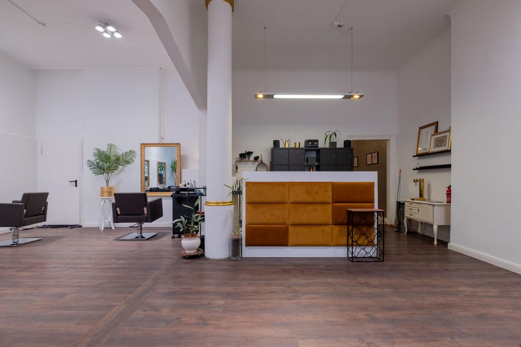 Ein moderner Friseursalon mit braunen Friseurstühlen, einem Empfangstresen mit orangefarbenen Polstern und weißen Wänden.