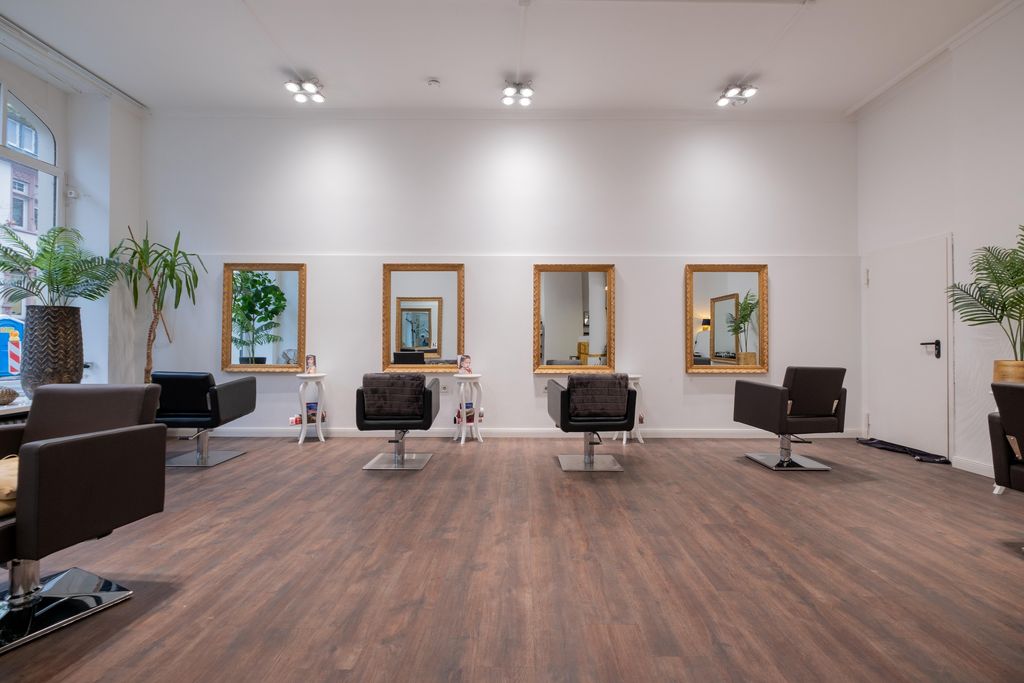 Moderner Friseursalon mit mehreren Friseur-Stühlen vor großen Spiegeln, Holzfußboden und Pflanzen an den Wänden.