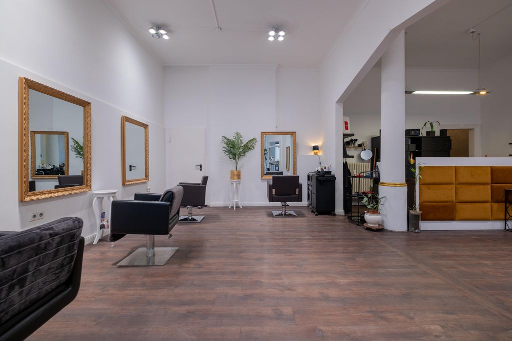 Moderner Friseursalon mit Holzboden, großen Spiegeln an weißen Wänden und schwarzen Friseurstühlen in einem hellen, geräumigen Raum.