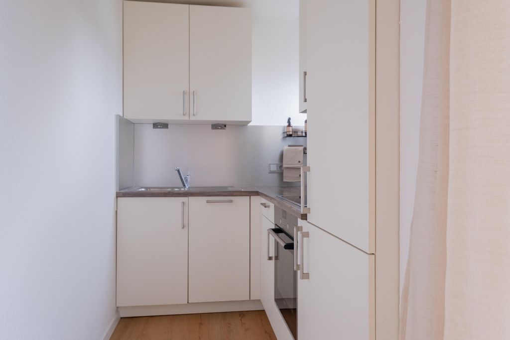 Kleine, moderne Küche mit weiß-lackierten Schränken, Spüle, Backofen und Holzfußboden.