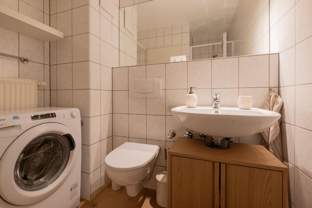 Kleines Badezimmer mit Waschmaschine, wandhängendem WC, Waschbecken auf Holzunterschrank und großem Spiegel.