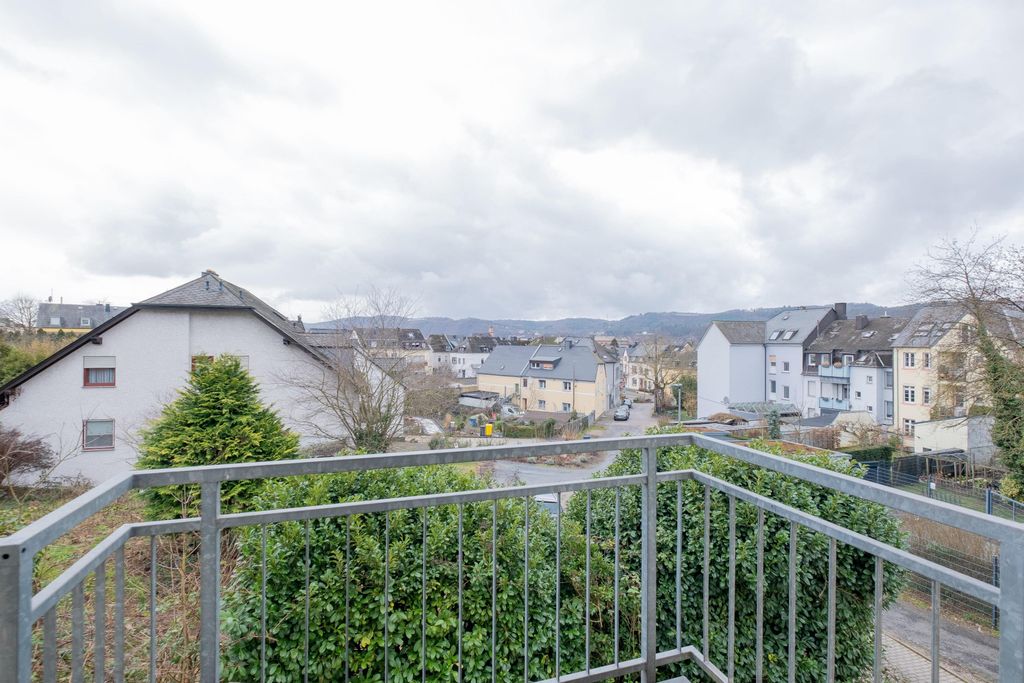 Blick von einem Balkon auf eine Wohnstraße mit mehrstöckigen Häusern bei bewölktem Himmel.