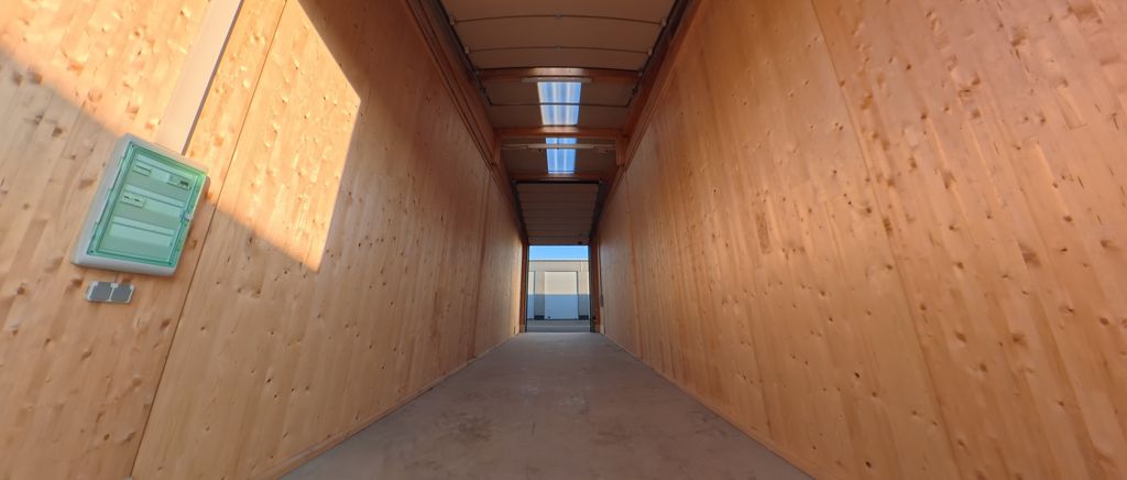 Ein langer, enger Durchgang mit Holzwänden und mehreren Deckenfenstern, der auf einen offenen Bereich mit Blick auf den Horizont führt.