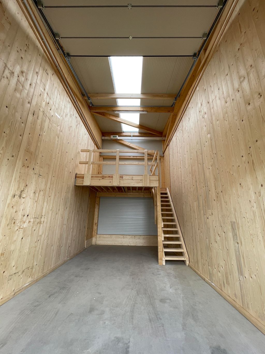 Innenraum eines schmalen Lagerraums mit Holzwänden, einer hohen Decke mit Dachfenstern und einer kleinen Holzemporatreppe an der Rückwand.
